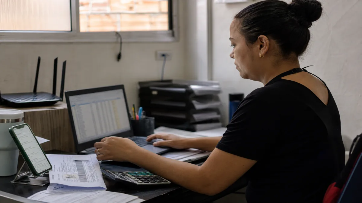Empresária de microempresa em São Paulo gerenciando contabilidade online no notebook e verificando documentos
